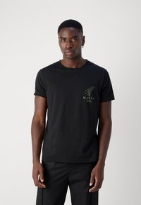 Black cotton t-shirt with short sleeves, featuring a green wing logo and "MAKIA CO." text on the left chest. Simple design and classic fit.