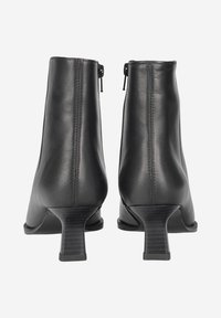 Bottines en cuir noir à talon tapered, avec des fermetures éclair latérales et une texture lisse. Design structuré, avec des détails de couture verticale.