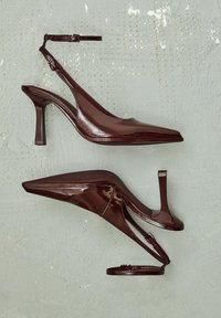 Bordo lakirani slingback sandali s izoštrenim vrhom, tankim remenčićem oko članaka i srednje visokim stiletto potplatom. Teksturirani potplat.
