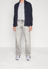 Námořnický pletený kardigan se dřevěnými knoflíky, světle šedé tričko s kulatým výstřihem, světle šedé volné džíny a bílé tenisky s černými detaily.