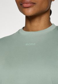 Mátově zelené tričko s kulatým výstřihem a krátkými rukávy, s jemným logem "BORG" na hrudi ve stejné barvě. Měkká, přiléhavá tkanina.