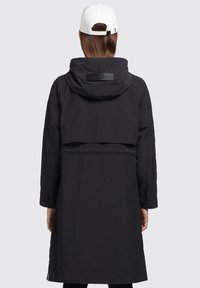 Manteau noir avec capuche, taille ajustable et détail de logo distinctif. Tissu lisse avec des manches longues et une silhouette décontractée.