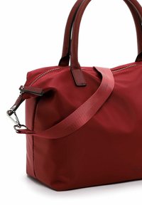 Raudona nailono rankinė su dviem trumpomis rankenomis ir nuimamu peties diržu. Turi viršutinį užtrauktuką ir plokščią dugną. Lygi tekstūra.