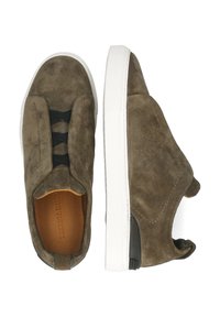 Zapatos de ante marrón sin cordones con una suela de goma blanca y detalles elásticos negros. Presentan una textura suave y un diseño de punta redondeada.