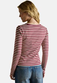 Garā piedurkņu krekls ar bordo un krēmkrāsas horizontālām svītrām, ar pieguļošu dizainu un ribota tekstūra. Aizmugures skatījumā ir apaļa kakla izgriezums.