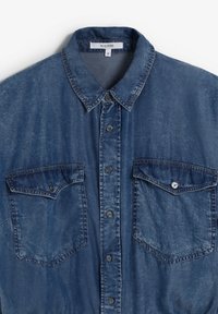 Chemise en denim bleu foncé avec un devant boutonné, un col pointu, et deux poches poitrine avec rabats et détails de coutures visibles.