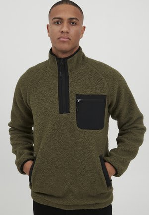 Olive green fleece pullover with a black zippered chest pocket, side pockets, high collar, and textured fabric. Features raglan sleeves.