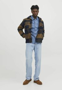 Ruudullinen takki ruskean ja laivastonsinisen sävyissä, kerroksittain denimpuseron päällä. Vaaleansiniset farkut; ruskeat liukuhousut. Yksinkertainen muotoilu nappikiinnityksellä.