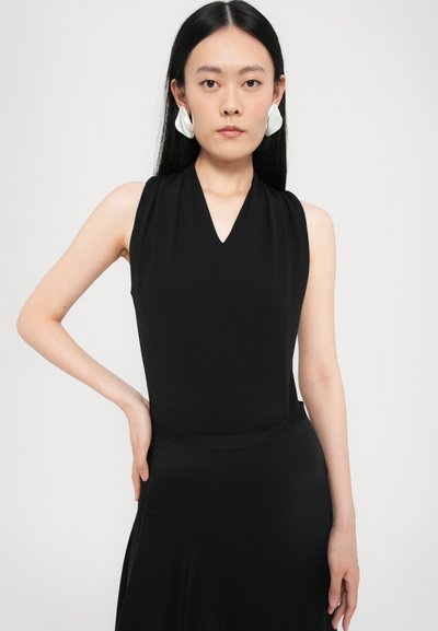 Black sleeveless top with a V-neck design, featuring smooth fabric and a fitted silhouette. Model wearing large white statement earrings.