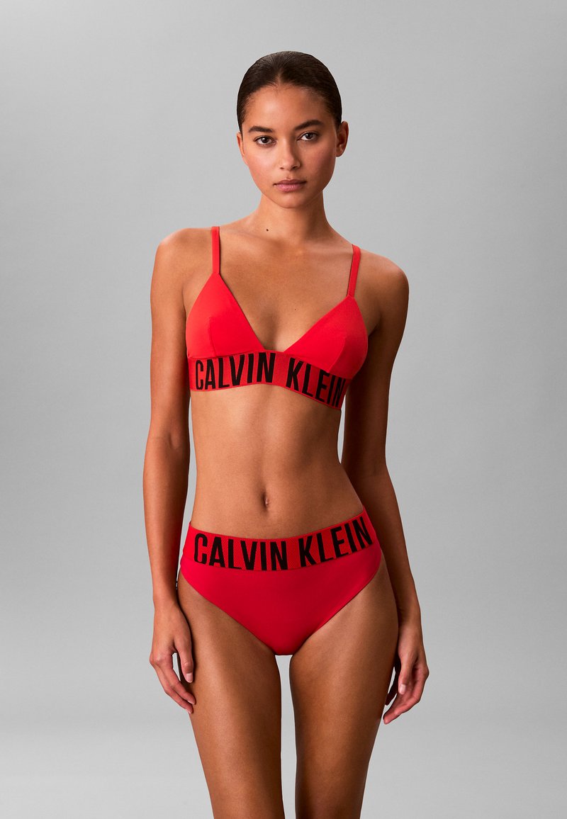 Completo bikini rosso composto da un reggiseno triangolare con spalline sottili e un abbinato slip a vita alta, entrambi contrassegnati dal testo nero "CALVIN KLEIN".