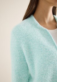 Cardigan bleu clair, doux au toucher, avec une texture pelucheuse, conçu avec une ouverture devant et une coupe ample. Il présente un motif de tricot délicat pour plus de détails.