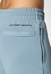 Lyseblå sporty shorts med elastisk talje, sidelomme og 'Jordan Sport' logo trykt i sort på ryggen.