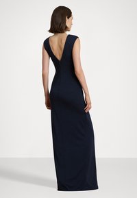 Tamsiai mėlyna, be rankovių ilga suknelė su giliu V formos nugaros iškirpimu, prigludusio dizaino ir užtrauktuku nugaroje. Sklandus audinys ir pilno ilgio siluetas.