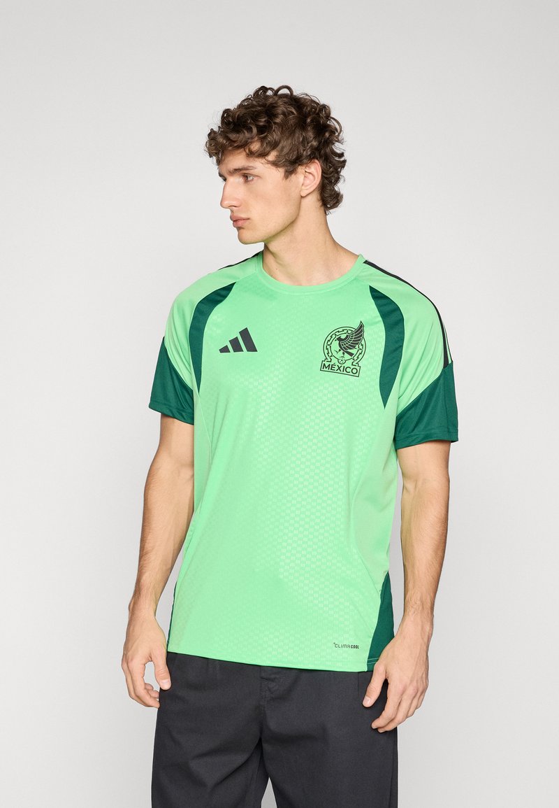 Light green athletic shirt with dark green accents, featuring a circular Mexican emblem, Adidas logo, and textured fabric. Short sleeves.