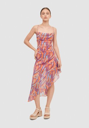 Vestido asimétrico con tirantes finos, que presenta un vibrante patrón de hojas en naranja, púrpura y azul sobre una tela transparente.