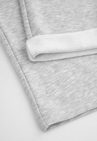 Szary materiał z melanzowanym wzorem, z białym tkanym wykończeniem. Widoczny złożony brzeg, ukazujący staranne szycie i gładkie wykończenie.