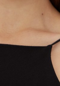 Haut noir sans manches avec une texture lisse et mate et un décolleté droit. Des bretelles fines relient le tissu aux épaules.