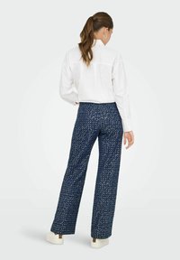 Chemise blanche à manches longues, associée à un pantalon large à motifs navy avec un design texturé et de subtils éclats blancs.
