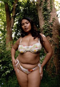 Bikini-setti, jossa on vaalenvärisiä kukkakuoseja, jossa on pehmustettu toppi säädettävillä olkaimilla ja solmittavat sivut alaosassa, asetettuna rehevään vihreään ympäristöön.