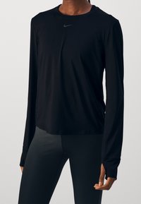 Černé atletické tričko s dlouhým rukávem vyrobené z lehké látky, s kulatým výstřihem a jemným šedým logem na hrudi.