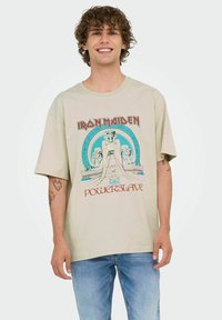 Camiseta de algodón beige con un diseño gráfico de arquitectura egipcia, texto "Iron Maiden" y "Powerslave" en rojo en la parte inferior.