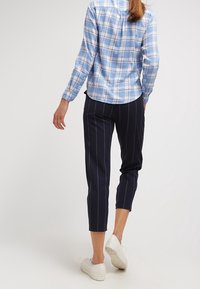 Světlomodrá kostkovaná košile na knoflíky s dlouhými rukávy, doplněná tmavě modrými zkrácenými kalhotami s vertikálními bílými pruhy a bílými teniskami.