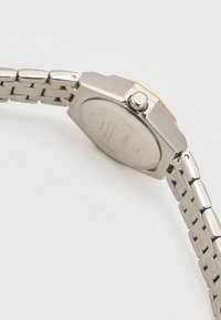 Sølvrækket armbåndsur med rektangulært urkasse, rustfrit stålværk og synlig krone. Bagsiden er glat med indgraverede detaljer.