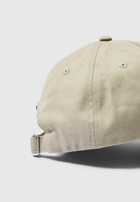 Cappellino da baseball beige con texture in tessuto, visiera curva e cinturino regolabile con accessori in metallo. Presenta fori di ventilazione e un bottone in alto.