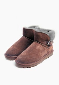 Stivaletti alla caviglia in suede marrone con una morbida fodera in pelliccia grigia, accentuati da una fascia laterale con fibbia metallica e una suola in gomma testurizzata.