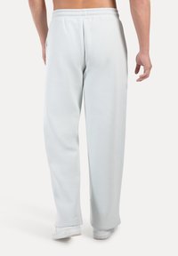 Pantalones de chándal azul claro con un corte relajado, cinturilla elástica y bolsillos laterales, mostrados desde la parte posterior. Textura de tejido suave y diseño de pierna recta.