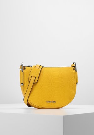 Sac bandoulière Calvin Klein en cuir jaune texturé avec bandoulière ajustable et garniture argentée, présenté sur un socle blanc.