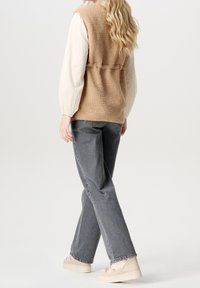 Beige Fleeceweste mit einer strukturierten weißen Langarmunterlage, kombiniert mit grauen Jeans und hellen Sneakern.