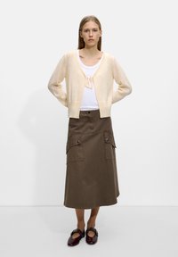 Jasno beżowy kardigan wykonany z miękkiego materiału, zapinany na troczek. W połączeniu z khaki spódnicą do kolan z dwoma przednimi kieszeniami. Ciemnoczerwone buty.