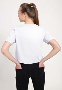 Witte korte mouwen t-shirt met een ontspannen pasvorm, van achteraf weergegeven. De drager combineert het met zwarte jeans met twee achterzakken.