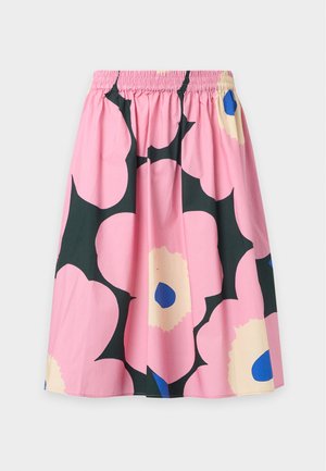 Femme portant une chemise blanche boutonnée, une jupe rose longueur genou avec un grand imprimé floral, des chaussettes blanches et des chaussures Mary Jane noires.