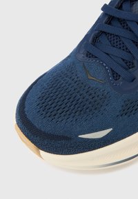 Αθλητικό παπούτσι σε ναυτικό μπλε με επάνω μέρος από διαπνέον δίχτυ, υφασμάτινη υφή, ανοιχτογκρι λεπτομέρειες και ευέλικτη λευκή σόλα με λαστιχένιο πέλμα.