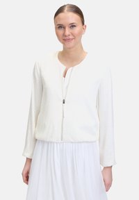 Weißer Zip-Up Bomberjacke aus strukturiertem Material, mit rundem Ausschnitt und langen Ärmeln. Auffällig sind der dezente Schimmer und der elastische Saum.
