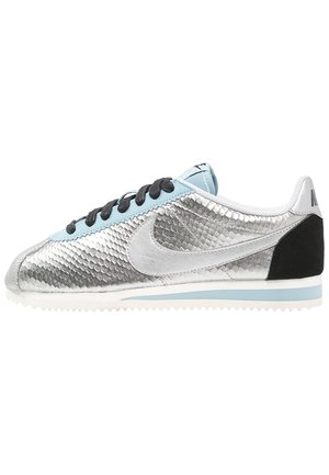 Scarpe da ginnastica argento con un design testurizzato a squame, accenti azzurri, tallone nero e suola bianca. Lacci neri completano il look.