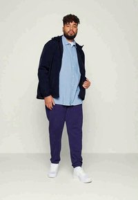 Jūras krāsas kapuci jaka virs gaiši zila krekla ar pogām, kombinēta ar purpura biksēm un baltām sporta kurpēm. Uzsvērta brīvā piegriezuma un ikdienišķā stila nozīme.