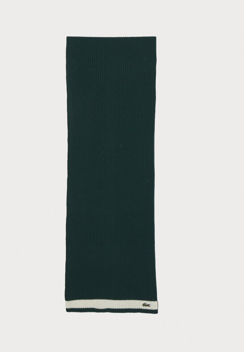 Grøn ribbet strikscarf med en lysecremefarvet stribet kant og en Lacoste logoetiket på kanten. Blød tekstur, forlænget rektangulær form.
