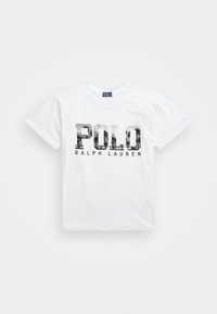 Valkoinen puuvillapaita, jossa on suuri "POLO" -grafiikka mustana ja harmaana, ja "RALPH LAUREN" pienemmällä tekstillä alla. Lyhyet hihat, pyöreä kaula-aukko.