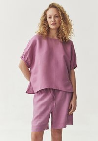 Top in lino lilla chiaro con maniche corte e spacchi laterali, abbinato a pantaloni corti con coulisse dello stesso colore. Tessuto morbido con una vestibilità rilassata.