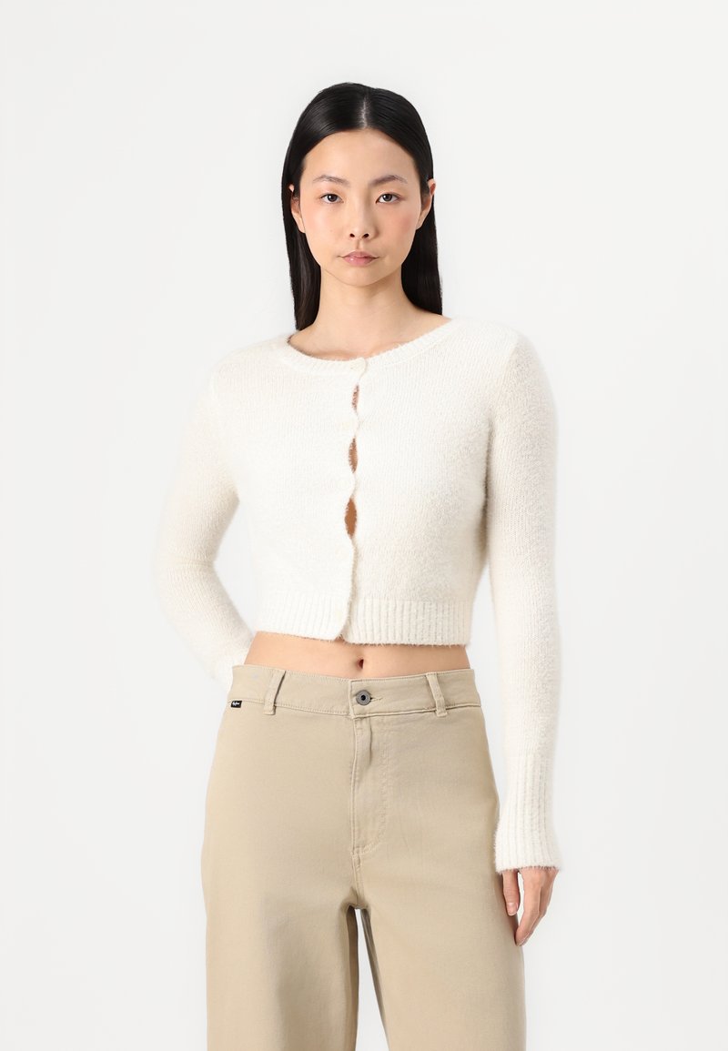 Weißer, verkürzter Cardigan mit geripptem Saum und langen Ärmeln, runder Ausschnitt und fünf Knopfverschlüssen vorne.