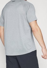 Camiseta deportiva de color gris claro fabricada con tejido que absorbe la humedad, con mangas cortas y un escote redondo, con un sutil logotipo de la marca en la parte trasera.