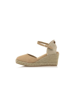 Zapato cuña beige de espadrille con un talón tejido texturizado y correa para el tobillo, con un diseño de punta redonda. Parte superior hecha de un material suave similar al ante.