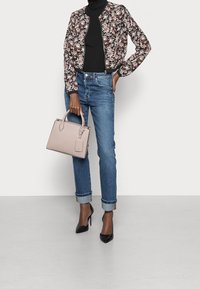 Blumen-Bomberjacke, schwarzer Rollkragenpullover, blaue, hochgekrempelte Jeans, schwarze spitze Pumps und eine hellrosa Handtasche mit Obergriffen und Anhänger-Detail.