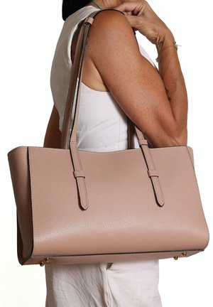 Vrouw in een wit mouwloos shirt met een grote beige boodschappentas met dubbele schouderbanden over haar arm.