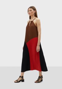 Abito maxi a plissé con blocchi di colore marrone, rosso e nero, scollatura a chiave e spalline sottili. Indossato con sandali neri con borchie.