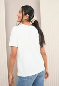 T-shirt blanc à manches courtes avec un col rond, associé à un jean bleu clair. Tissu en coton doux avec un design simple, coupe décontractée.