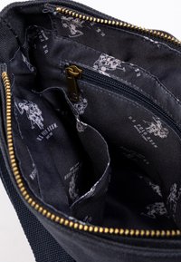 Interno della borsa in tessuto blu navy con più scomparti, dotato di una cerniera dorata e di una fodera in tessuto nero a motivo.